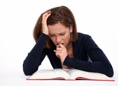 woman appears stressed while looking at a book, she is biting the side of her pointer finger nervously