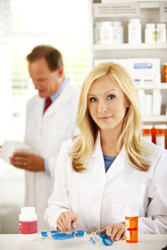 female pharmacist working with pills while facing camera, male pharmacist in background