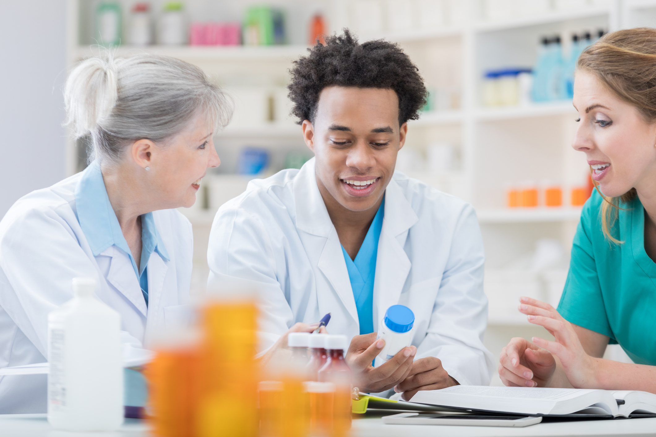 two female and one male pharmacist discussing the medicine bottle in the male's hand