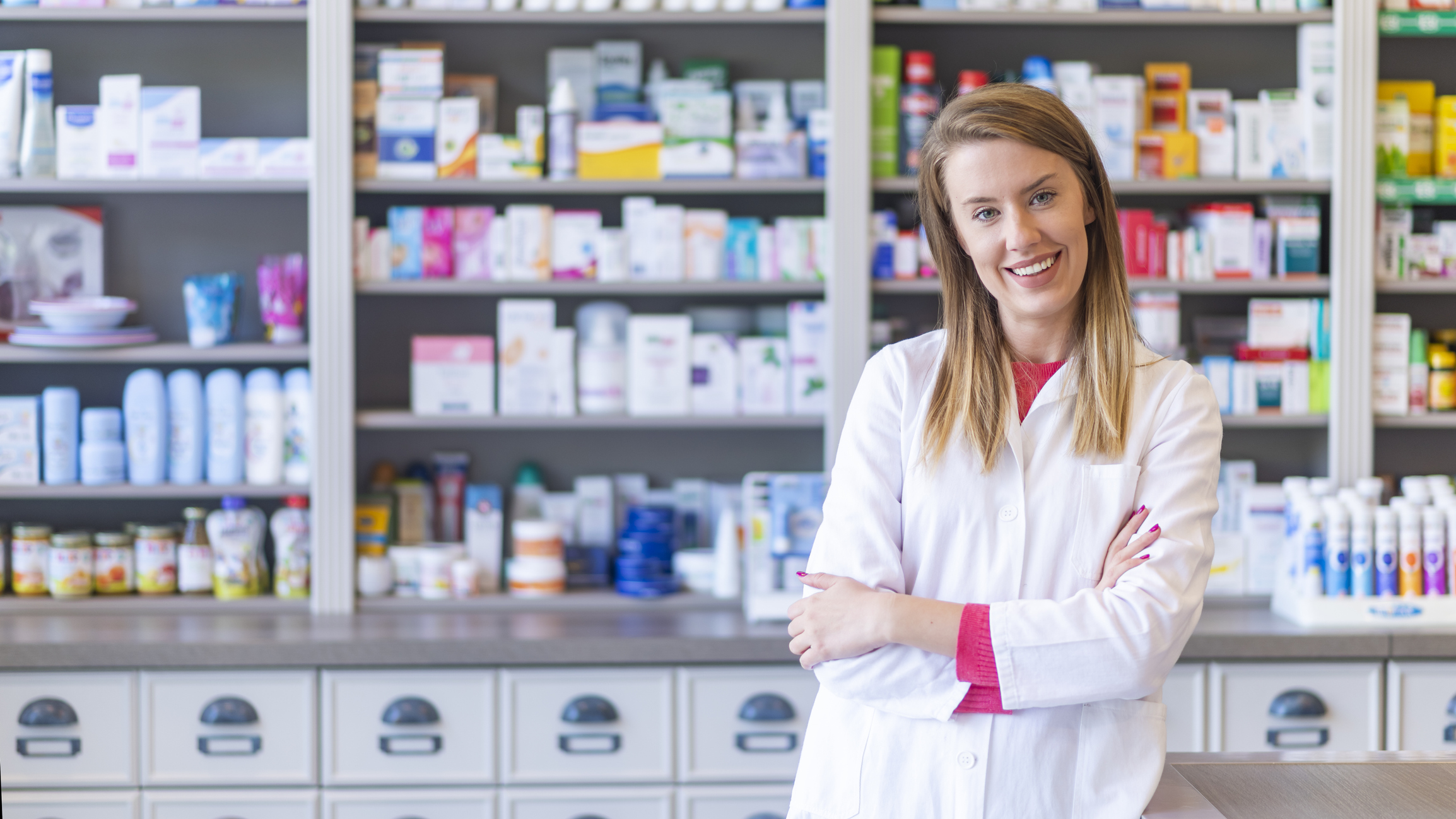 woman in labcoat standing in drugstore / pharmacy