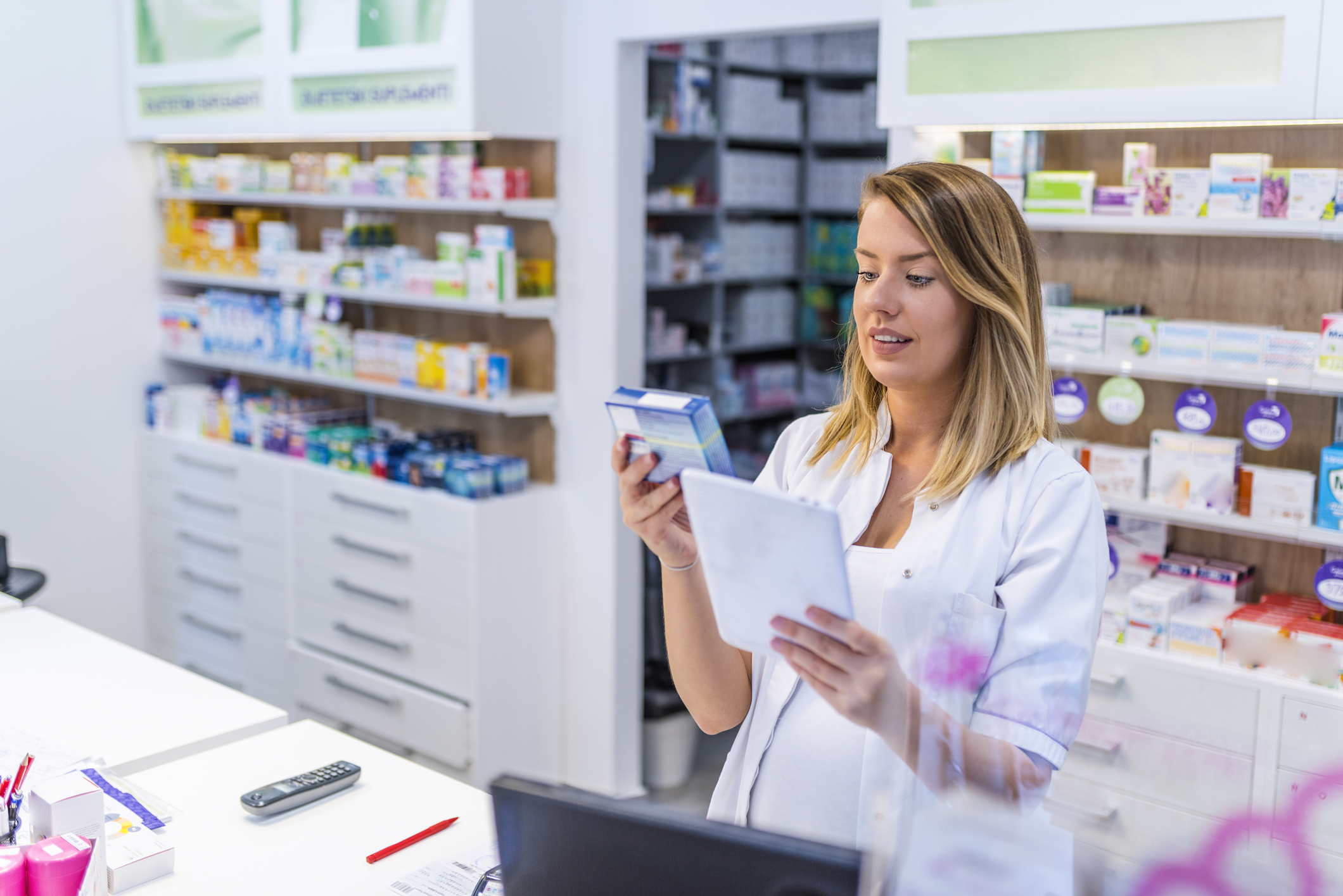 Young pharmacist holding a tablet and box of medications.