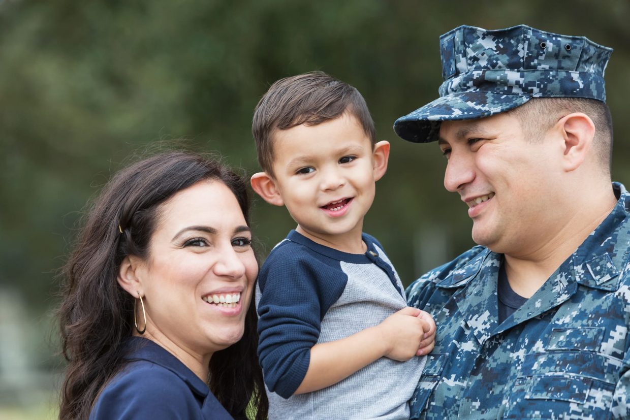 Man wearing Navy camouflage uniform carrying a small boy with a smiling woman