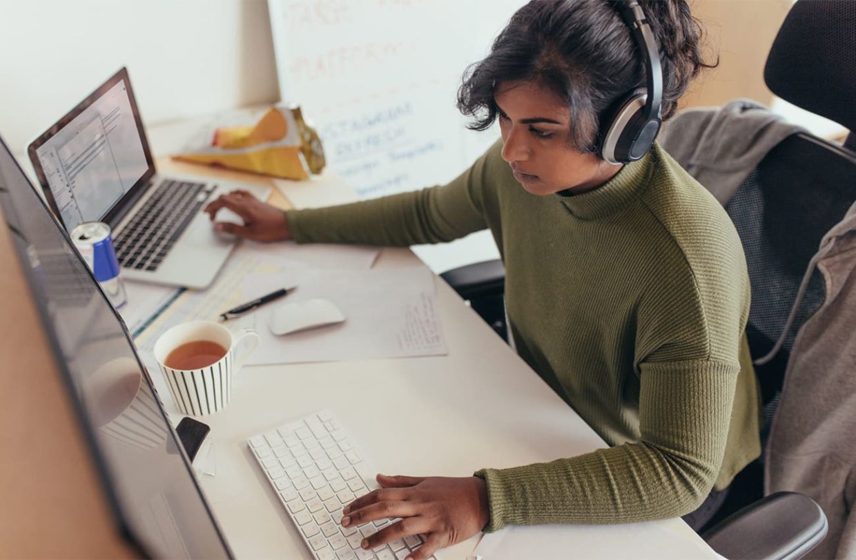 Woman sitting at workstation while typing on two different computer keyboards simultaneously.