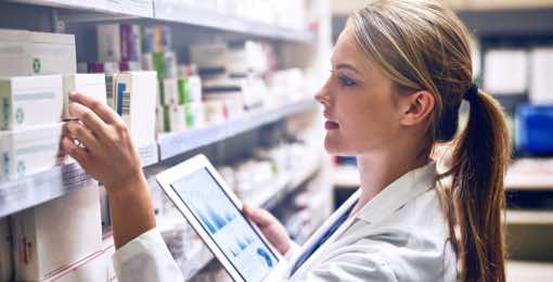 young woman wearing lab coat looking holding an ipad and looking at boxes